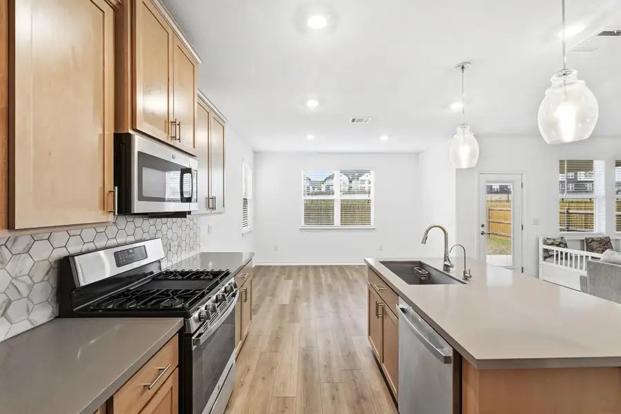 Kitchen with stainless steel appliances, a center island with sink, light wood-style flooring, tasteful backsplash, and decorative light fixtures