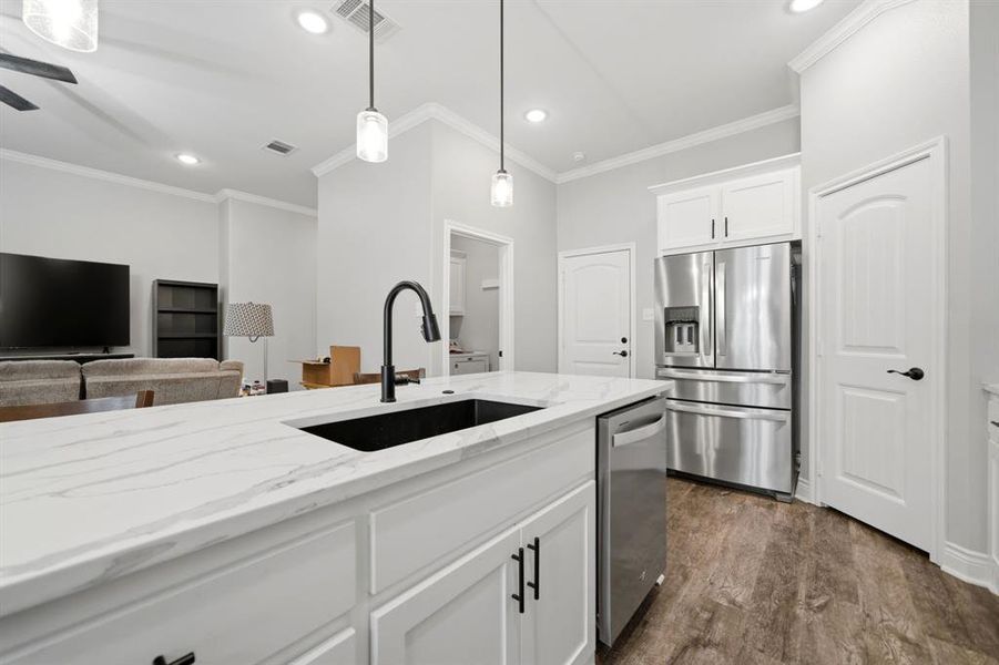 Kitchen featuring white cabinetry, stainless steel appliances, light stone counters, decorative light fixtures, and dark wood finished floors