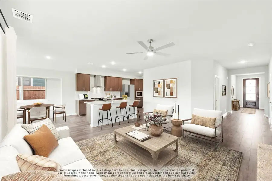 Open-concept living room with hardwood floors and ceiling fan, flowing into kitchen with dark wood cabinets and island seating