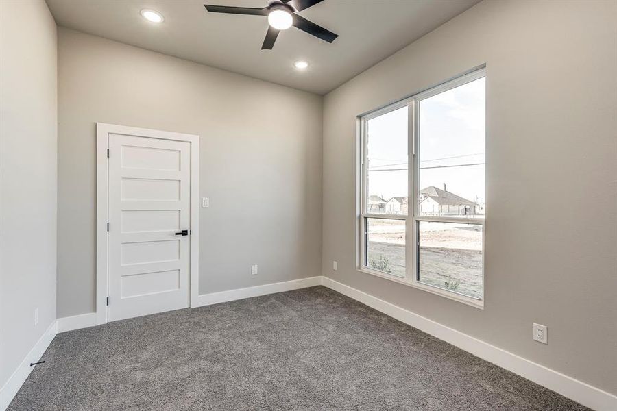 Spare room featuring plenty of natural light, a ceiling fan, dark colored carpet, and baseboards