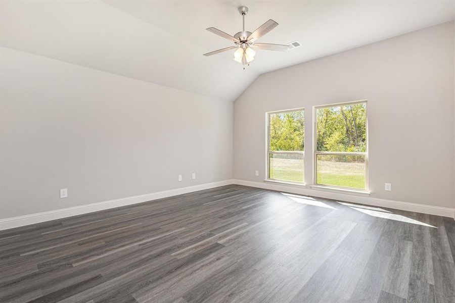 Empty room featuring dark wood-style flooring, lofted ceiling, and ceiling fan Empty room featuring dark wood-style flooring, lofted ceiling, and ceiling fan