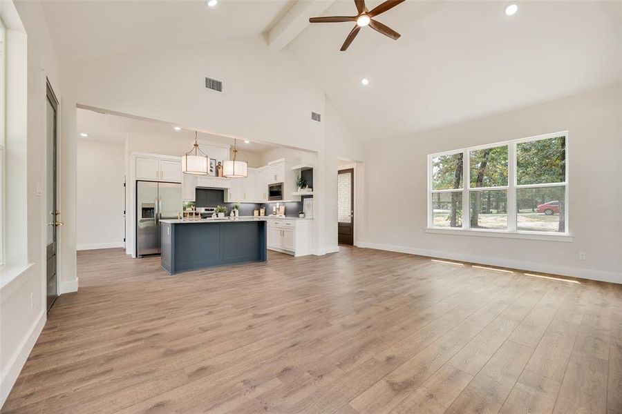 Unfurnished living room with light wood-type flooring, beam ceiling, recessed lighting, high vaulted ceiling, and ceiling fan