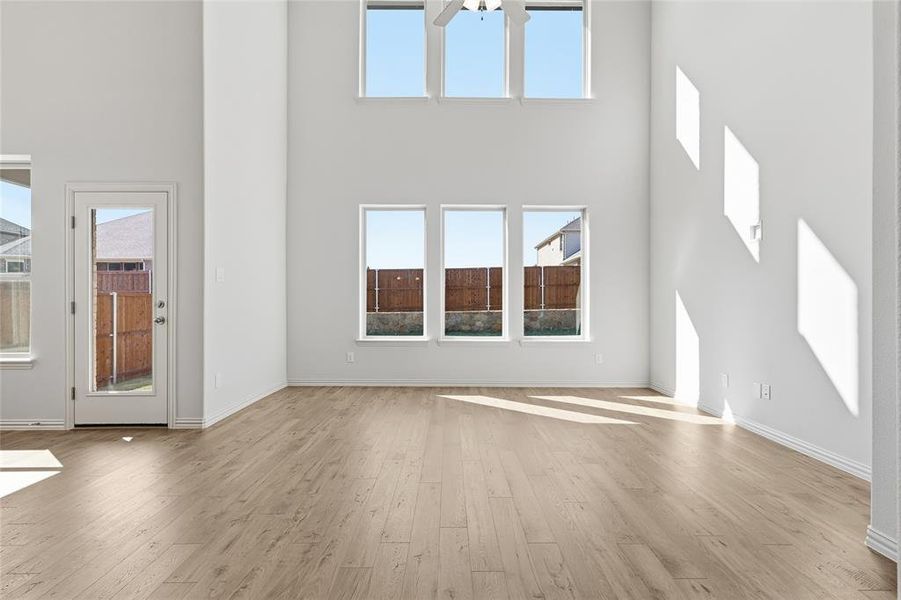 Unfurnished living room with light wood-style floors, healthy amount of natural light, and a high ceiling