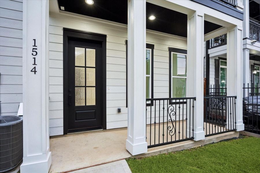 A welcoming covered entry introduces this contemporary residence with crisp white siding, bold black trim, and striking architectural details. The black front door with divided glass creates a polished focal point, while decorative iron railings add character to the porch. Recessed ceiling lights provide a warm glow, and the compact green space completes the clean, modern approach to the home. A welcoming covered entry introduces this contemporary residence with crisp white siding, bold black trim, and striking architectural details. The black front door with divided glass creates a polished focal point, while decorative iron railings add character to the porch. Recessed ceiling lights provide a warm glow, and the compact green space completes the clean, modern approach to the home.
