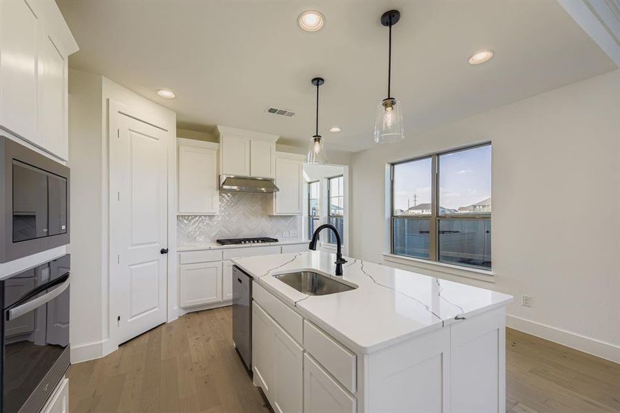 Kitchen with tasteful backsplash, light wood-style flooring, appliances with stainless steel finishes, a center island with sink, and recessed lighting