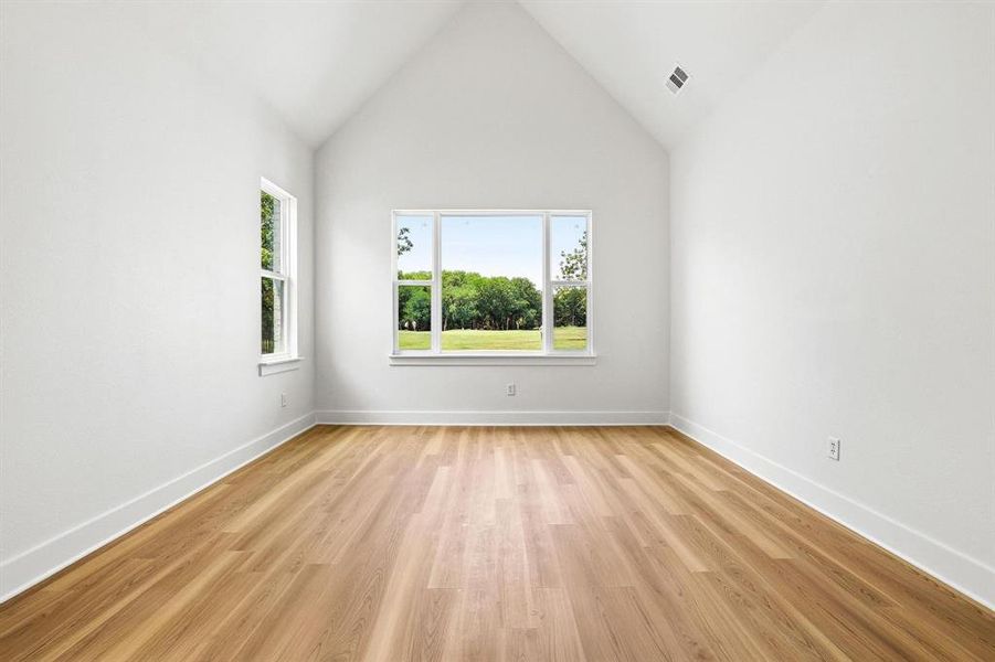 Vaulted ceiling room featuring wood-finish flooring, white baseboards, and multiple windows overlooking a green landscape Vaulted ceiling room featuring wood-finish flooring, white baseboards, and multiple windows overlooking a green landscape