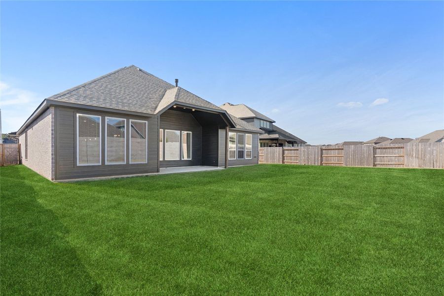 This wide view of the backyard highlights the generous green space and clean lines of the home’s rear elevation, offering plenty of room for outdoor entertaining, play, or future landscaping, all within a fully fenced setting that provides privacy and peace of mind.