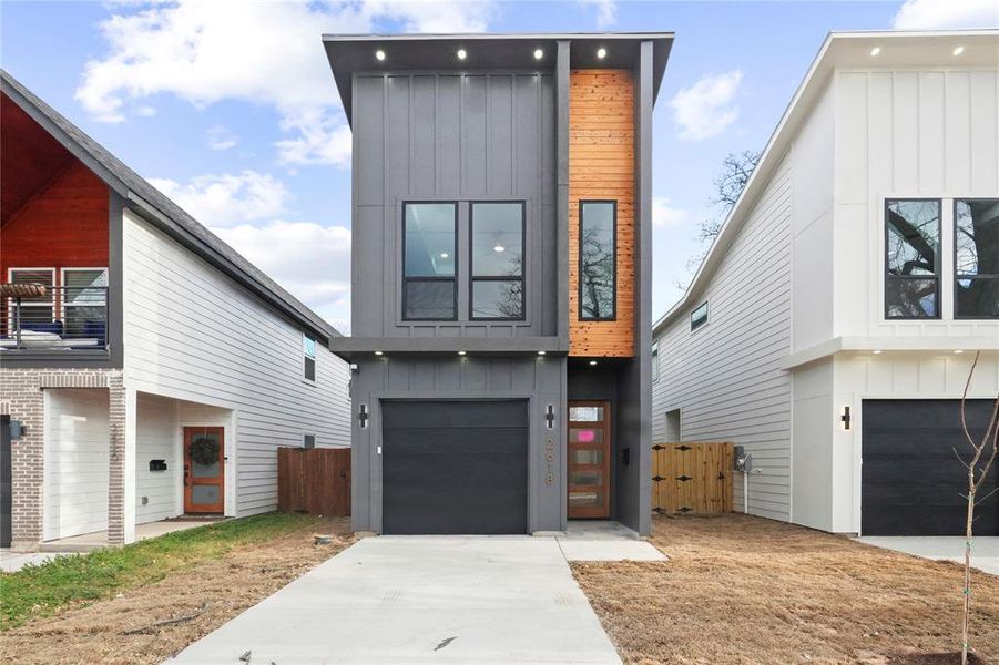 Contemporary house featuring board and batten siding, concrete driveway, an attached garage, a gate, and a balcony Contemporary house featuring board and batten siding, concrete driveway, an attached garage, a gate, and a balcony