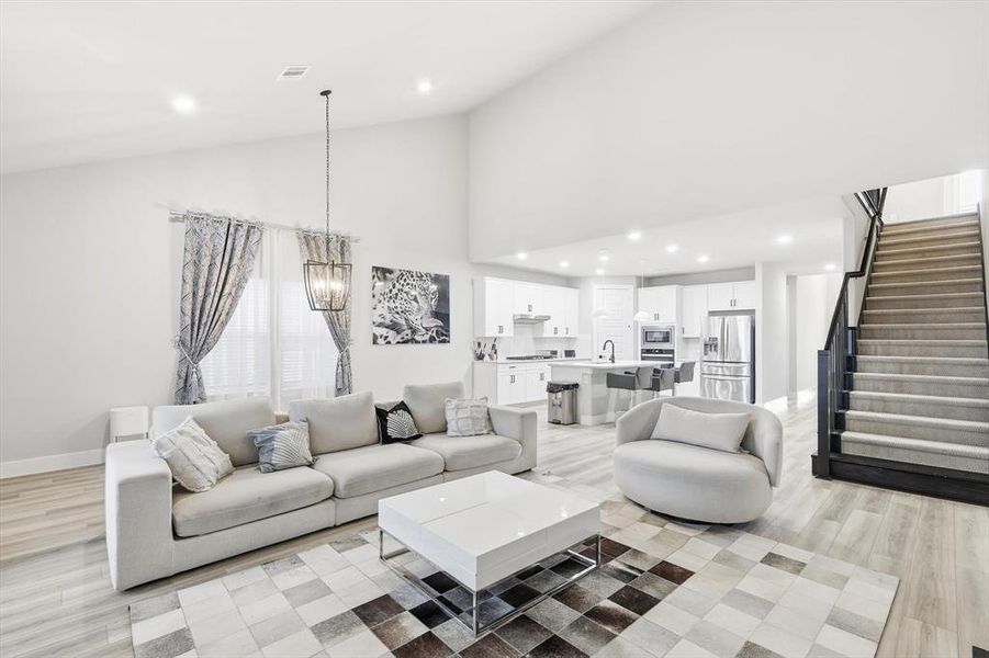 Living room featuring stairs, light wood finished floors, recessed lighting, high vaulted ceiling, and a chandelier
