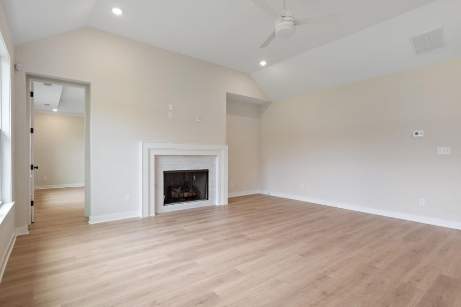 Vaulted ceiling with recessed lighting, wood-finish flooring, and a fireplace with a white mantel and tile surround Vaulted ceiling with recessed lighting, wood-finish flooring, and a fireplace with a white mantel and tile surround
