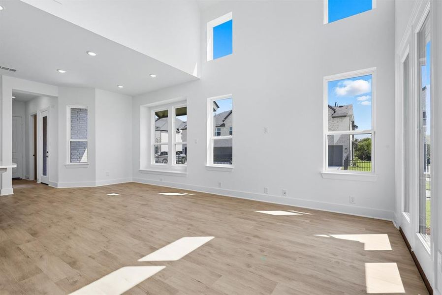 Unfurnished living room featuring light wood-style floors, healthy amount of natural light, a towering ceiling, and recessed lighting Unfurnished living room featuring light wood-style floors, healthy amount of natural light, a towering ceiling, and recessed lighting