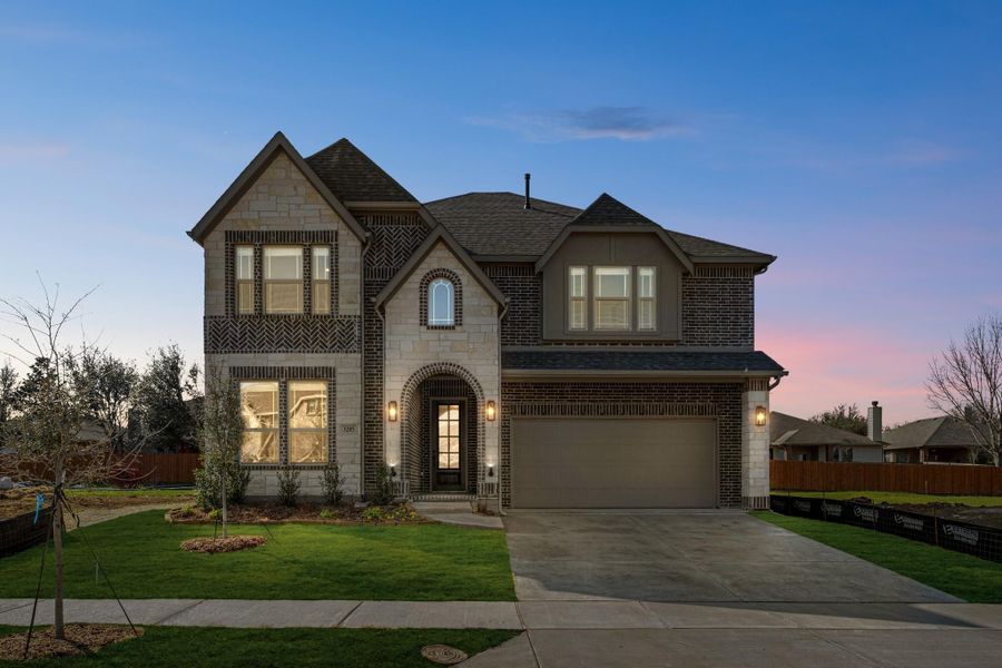 Two-story home with stone and brick exterior, arched entry, two-car garage, and green front lawn at dusk Two-story home with stone and brick exterior, arched entry, two-car garage, and green front lawn at dusk