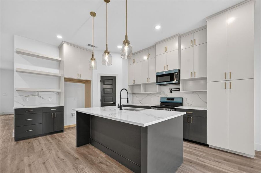 Modern kitchen featuring a central island with a waterfall countertop, contemporary pendant lighting, extensive white cabinetry, high-contrast dark lower cabinets, and wood-finish flooring Modern kitchen featuring a central island with a waterfall countertop, contemporary pendant lighting, extensive white cabinetry, high-contrast dark lower cabinets, and wood-finish flooring