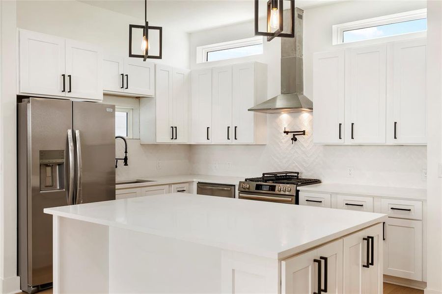 This is a modern kitchen featuring white cabinetry, stainless steel appliances, a gas stove with pot filler,  and a central island with a white countertop. It has a clean, contemporary design with a herringbone tile backsplash.