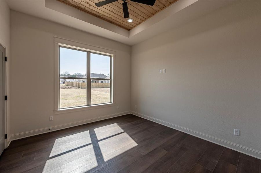 Empty room with a wooden tray ceiling, a ceiling fan, and dark wood-style floors Empty room with a wooden tray ceiling, a ceiling fan, and dark wood-style floors