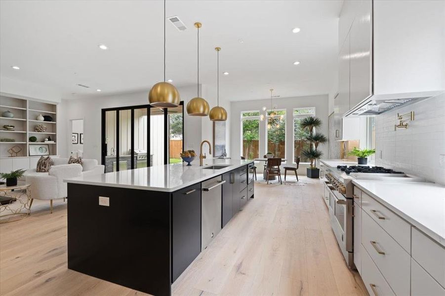 Kitchen with a center island with sink, hanging light fixtures, white cabinetry, and stainless steel appliances