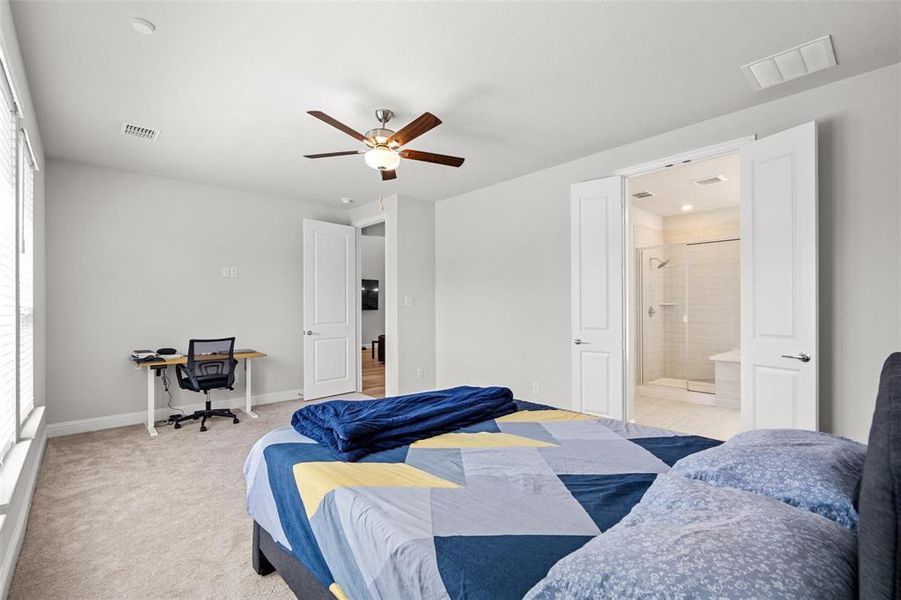 Bedroom with multiple windows, light carpet, ensuite bathroom, and ceiling fan