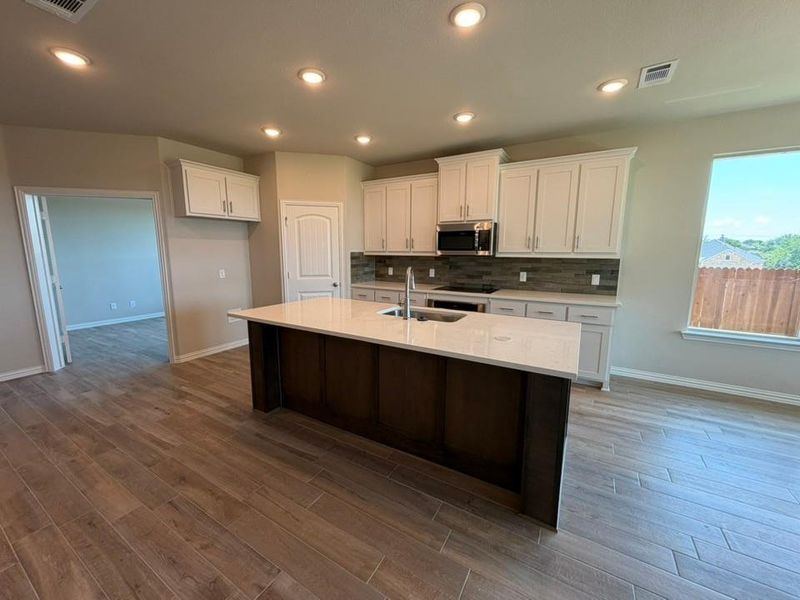 Kitchen featuring a center island, white cabinetry, integrated stainless steel appliances, wood-finish flooring, and a window