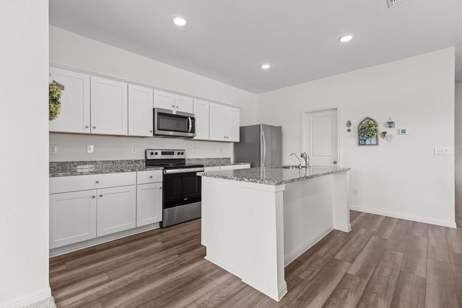 Kitchen with stainless steel appliances, white cabinets, light stone countertops, a kitchen island with sink, and dark wood-style flooring Kitchen with stainless steel appliances, white cabinets, light stone countertops, a kitchen island with sink, and dark wood-style flooring