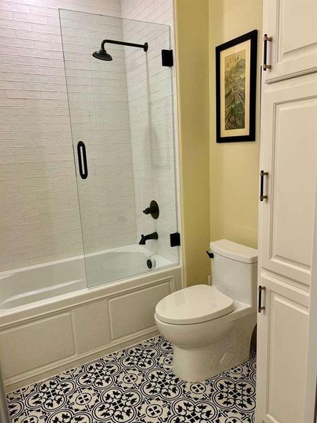 Bathroom with tile patterned flooring, combined bath / shower with glass door, and toilet