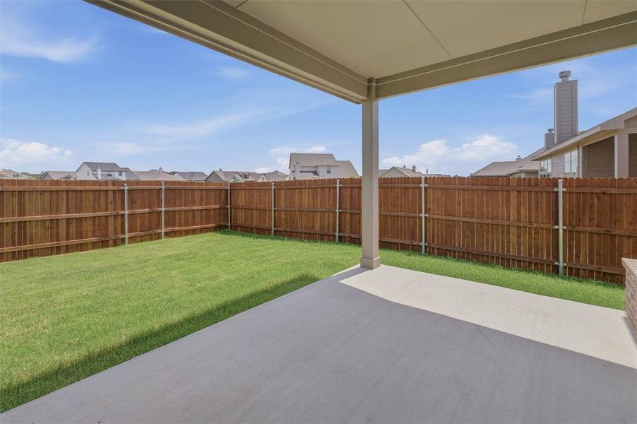 Covered concrete patio opening to a fenced rear yard with a manicured lawn