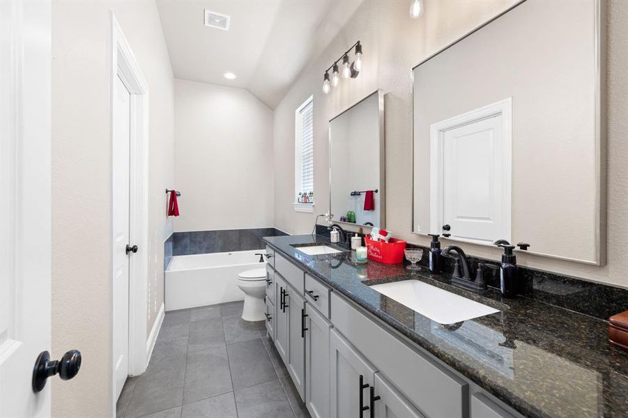 Bathroom with tile patterned flooring, a bath, lofted ceiling, toilet, and vanity