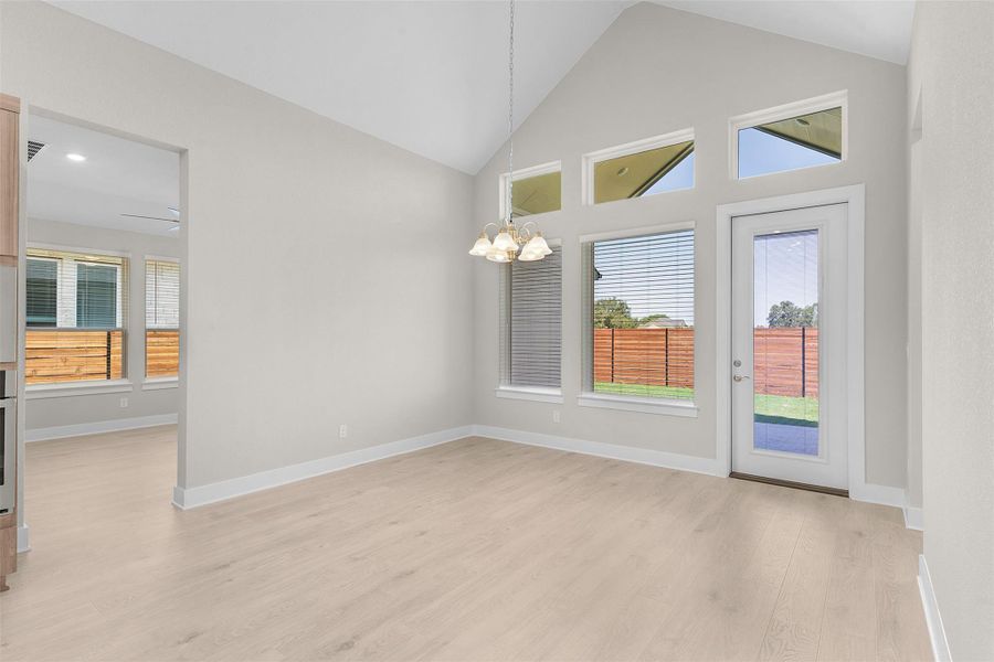 Unfurnished dining area featuring light wood-type flooring, high vaulted ceiling, and a chandelier Unfurnished dining area featuring light wood-type flooring, high vaulted ceiling, and a chandelier