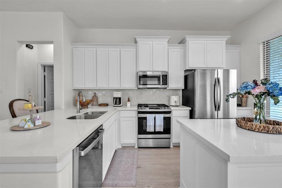 Bright kitchen featuring white cabinetry, light countertops, stainless steel appliances, a built-in microwave, and a double basin sink Bright kitchen featuring white cabinetry, light countertops, stainless steel appliances, a built-in microwave, and a double basin sink