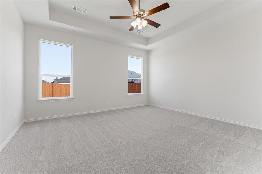Empty room with light colored carpet, a raised ceiling, and ceiling fan