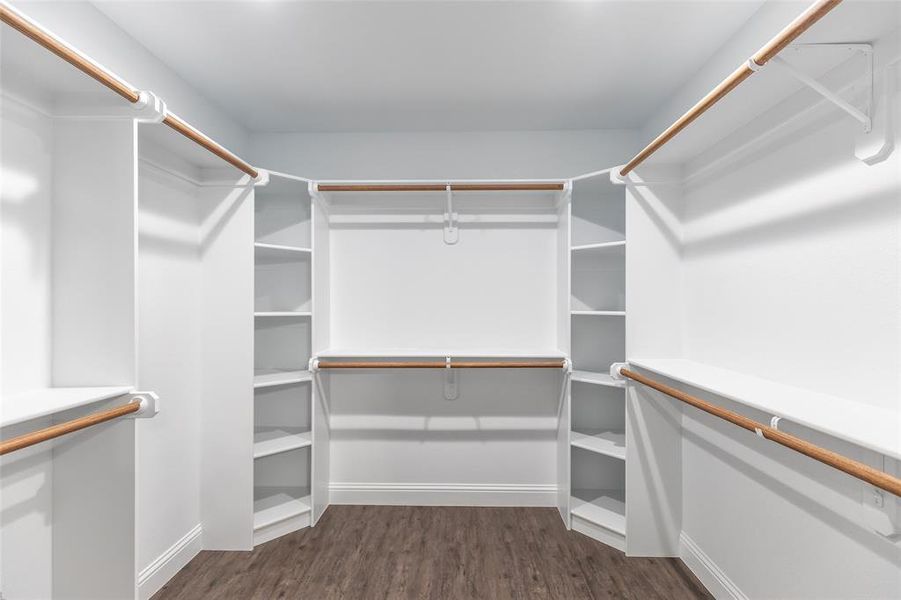 Walk-in closet featuring wood-finish flooring, white built-in shelving, white baseboards, and multiple hanging rods