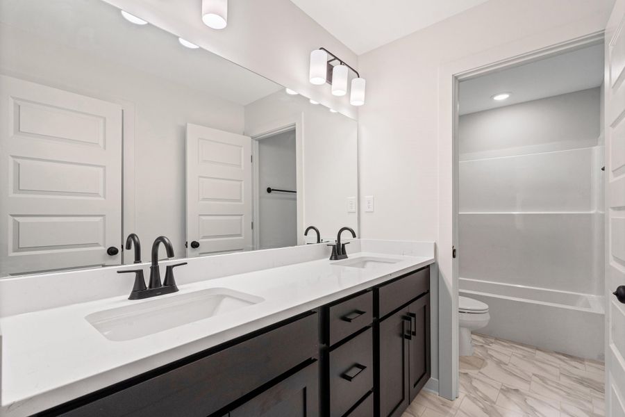 Bathroom featuring a dual vanity with dark wood-finish cabinetry and white countertops Bathroom featuring a dual vanity with dark wood-finish cabinetry and white countertops