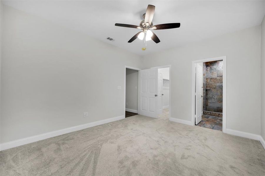 Unfurnished bedroom with connected bathroom, a spacious closet, visible vents, carpet floors, and baseboards Unfurnished bedroom with connected bathroom, a spacious closet, visible vents, carpet floors, and baseboards