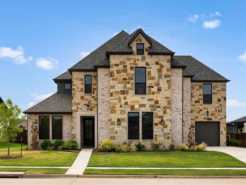 French country inspired facade featuring a shingled roof, stone siding, driveway, and a garage