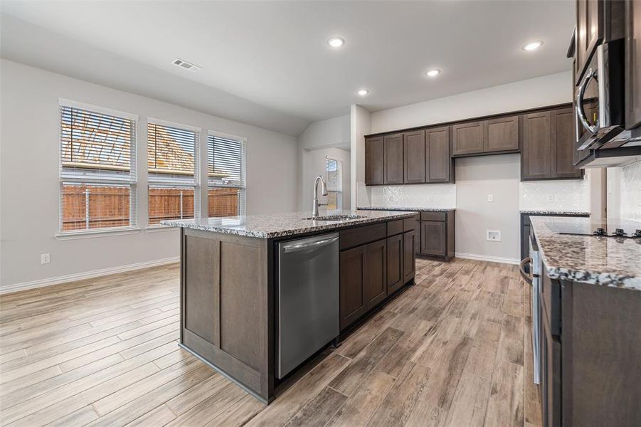 Kitchen featuring light stone countertops, dark brown cabinets, stainless steel appliances, recessed lighting, and a kitchen island with sink Kitchen featuring light stone countertops, dark brown cabinets, stainless steel appliances, recessed lighting, and a kitchen island with sink
