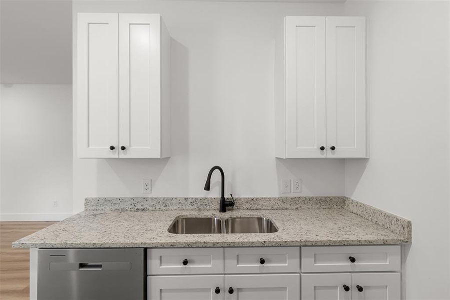 Kitchen with light stone countertops, white cabinetry, stainless steel dishwasher, and sink