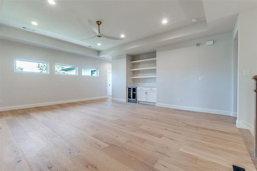 Unfurnished living room featuring a tray ceiling, light wood finished floors, recessed lighting, wine cooler, and a ceiling fan Unfurnished living room featuring a tray ceiling, light wood finished floors, recessed lighting, wine cooler, and a ceiling fan