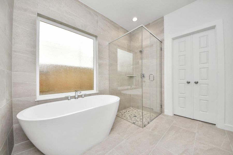 Indulge in a spa-like retreat within the confines of this primary bathroom. Delight in a spacious walk-in shower enveloped in stylish tile surround, unwind in a separate garden tub adorned with custom detailing. Sample photo of completed home with similar floor plan. Actual colors and selections may vary.