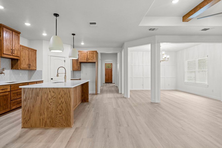 A pristine open-concept kitchen and living area features wood cabinets, pendant lighting, and light-toned flooring. A pristine open-concept kitchen and living area features wood cabinets, pendant lighting, and light-toned flooring.