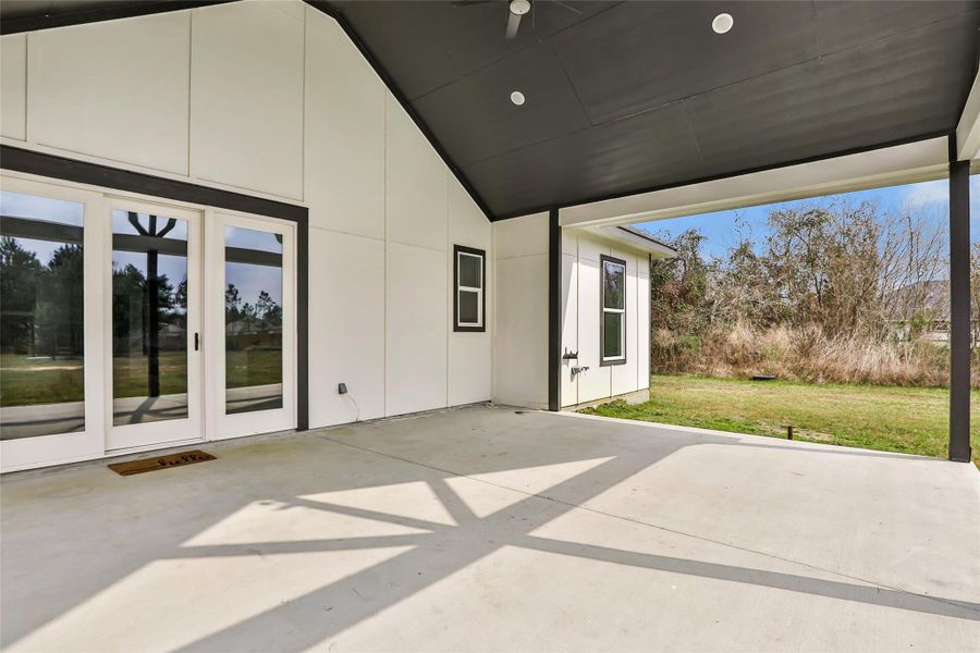 Spacious covered patio with modern design, featuring large glass doors and a view of a grassy backyard, ideal for outdoor relaxation and entertaining.