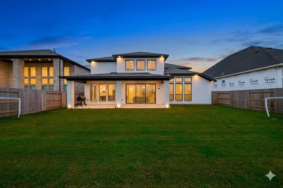 This photo showcases a modern two-story home with a spacious backyard. The exterior features large windows and a covered patio, perfect for outdoor living. The surrounding wooden fence offers privacy, and the yard is ideal for family activities. Photos have been virtually to help illustrate the potential of the nighttime looks.