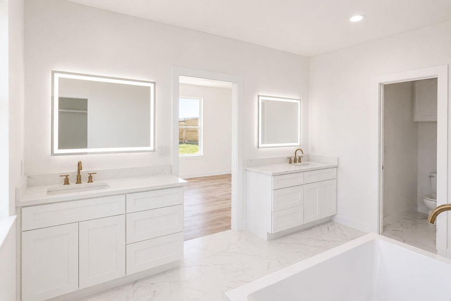 Dual vanities with illuminated mirrors enhance this generously sized primary bathroom.