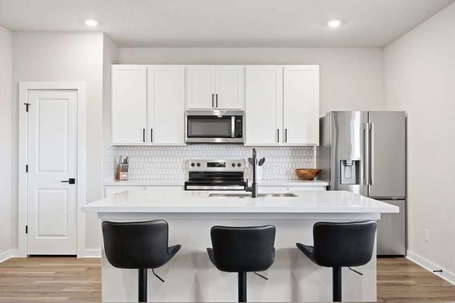 An open kitchen layout centers on a large island set over classic wood-style flooring. An open kitchen layout centers on a large island set over classic wood-style flooring.