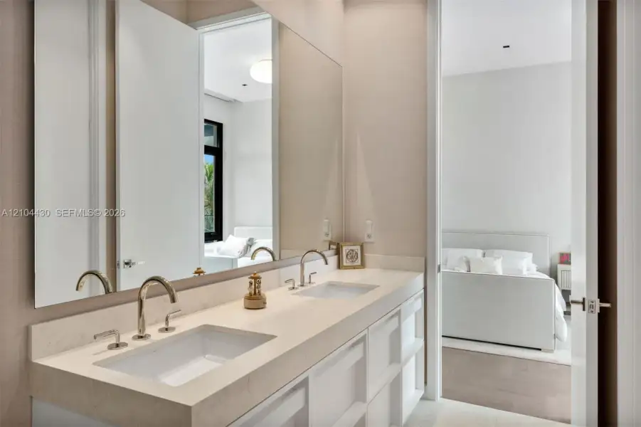 Dual-sink vanity with a solid-surface countertop, rectangular under-mount basins, polished metal gooseneck faucets, and a full-width wall mirror