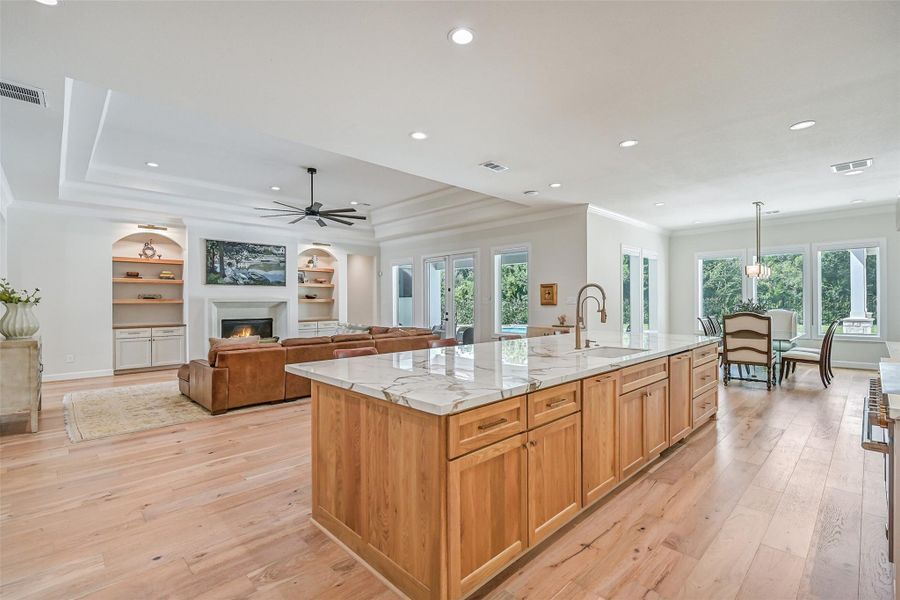 This view captures the scale of the open living space, with the massive Calacatta Macchia Vecchia-topped island overlooking the family room, gas-log fireplace and backyard pool beyond — all surrounded by beautiful wood flooring and abundant natural light.