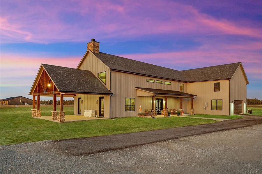Rear view of house with a patio, a shingled roof, a garage, a lawn, and a chimney