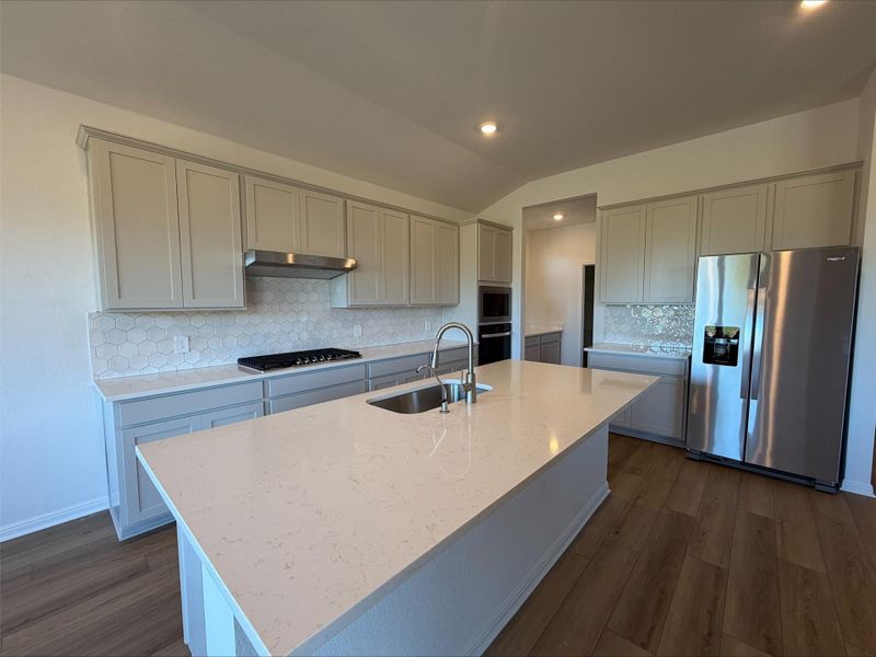 Kitchen featuring appliances with stainless steel finishes, vaulted ceiling, dark wood-style flooring, light stone counters, and backsplash