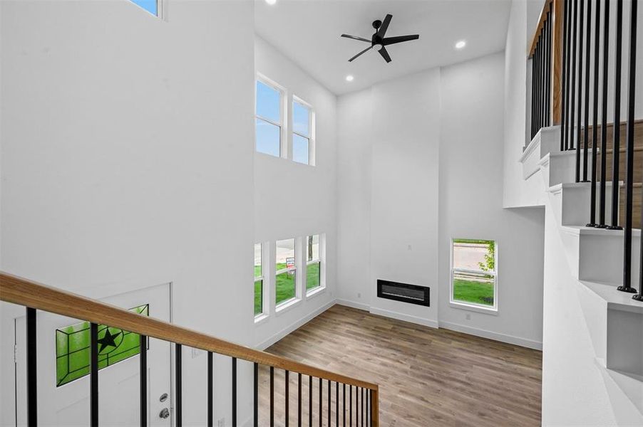 Unfurnished living room featuring ceiling fan, light wood-type flooring, and a high ceiling