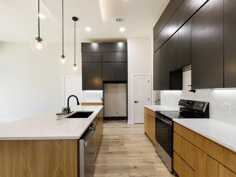 Kitchen featuring range with electric stovetop, light stone counters, hanging light fixtures, dishwasher, and modern cabinets