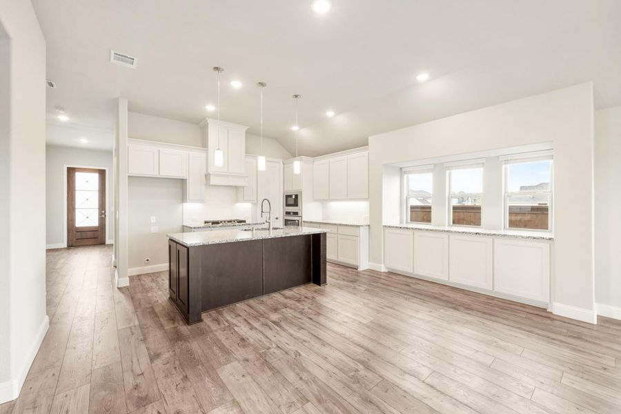 Open kitchen with white cabinets, dark island with granite countertop, and light wood floors Open kitchen with white cabinets, dark island with granite countertop, and light wood floors