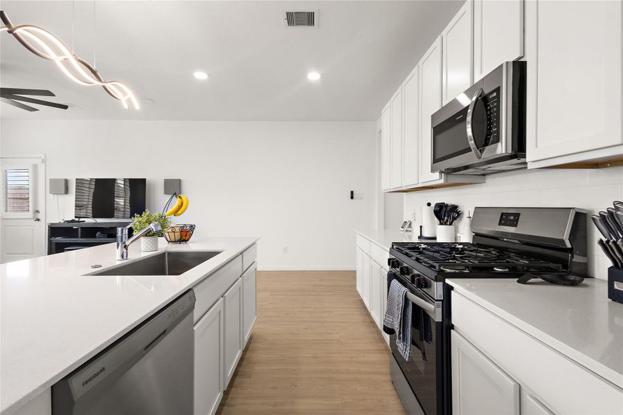 Modern kitchen with sleek white cabinetry, stainless steel appliances, and a large island with a sink. The space features recessed lighting and opens into a living area with light wood flooring, creating a bright and spacious atmosphere.